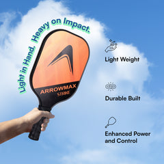 Orange and black pickleball paddle held by a hand with text highlighting features against a blue sky.